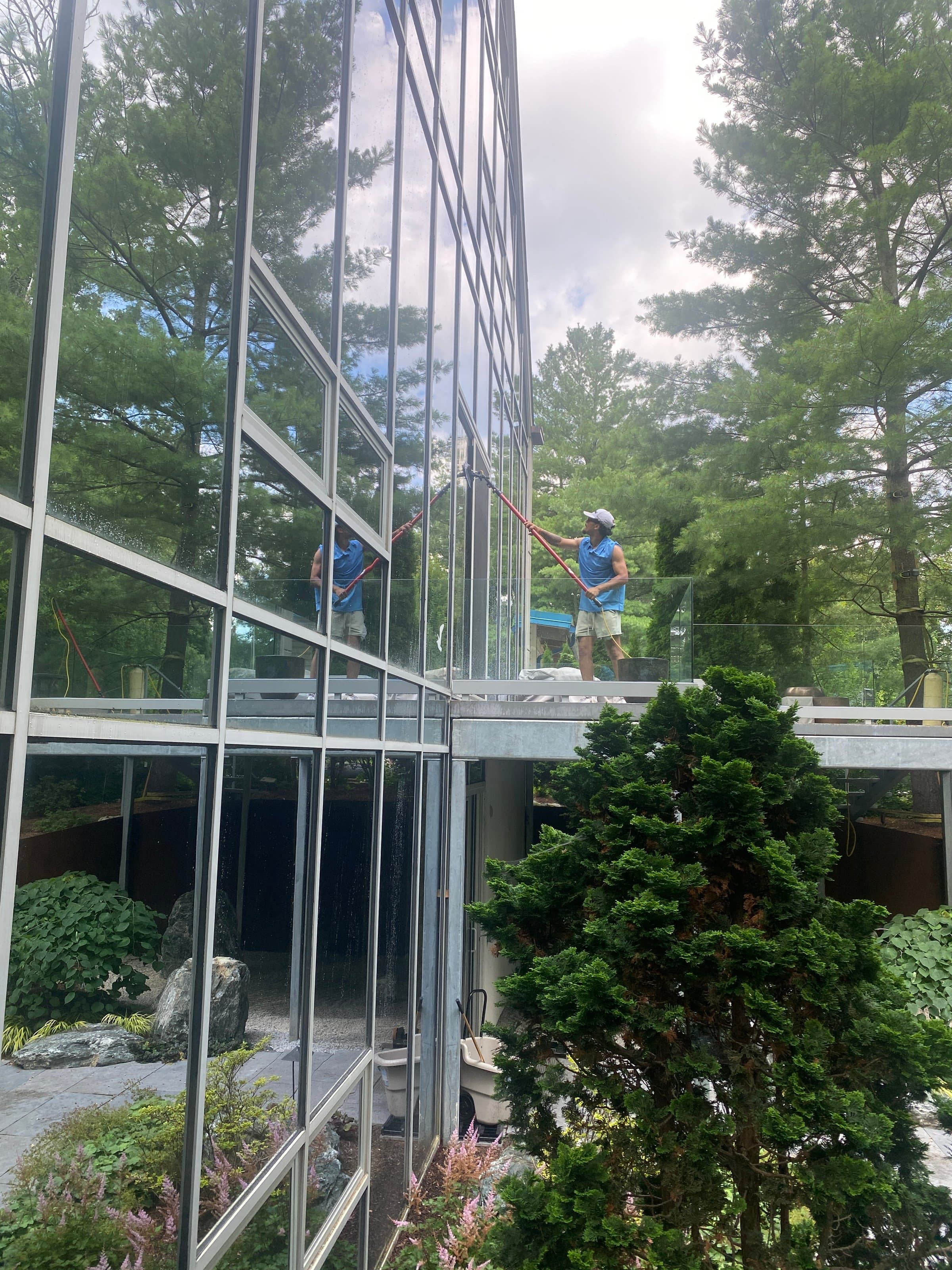 Super Shine Services technician cleaning floor-to-ceiling glass windows on a modern Metro Detroit home with a water-fed pole