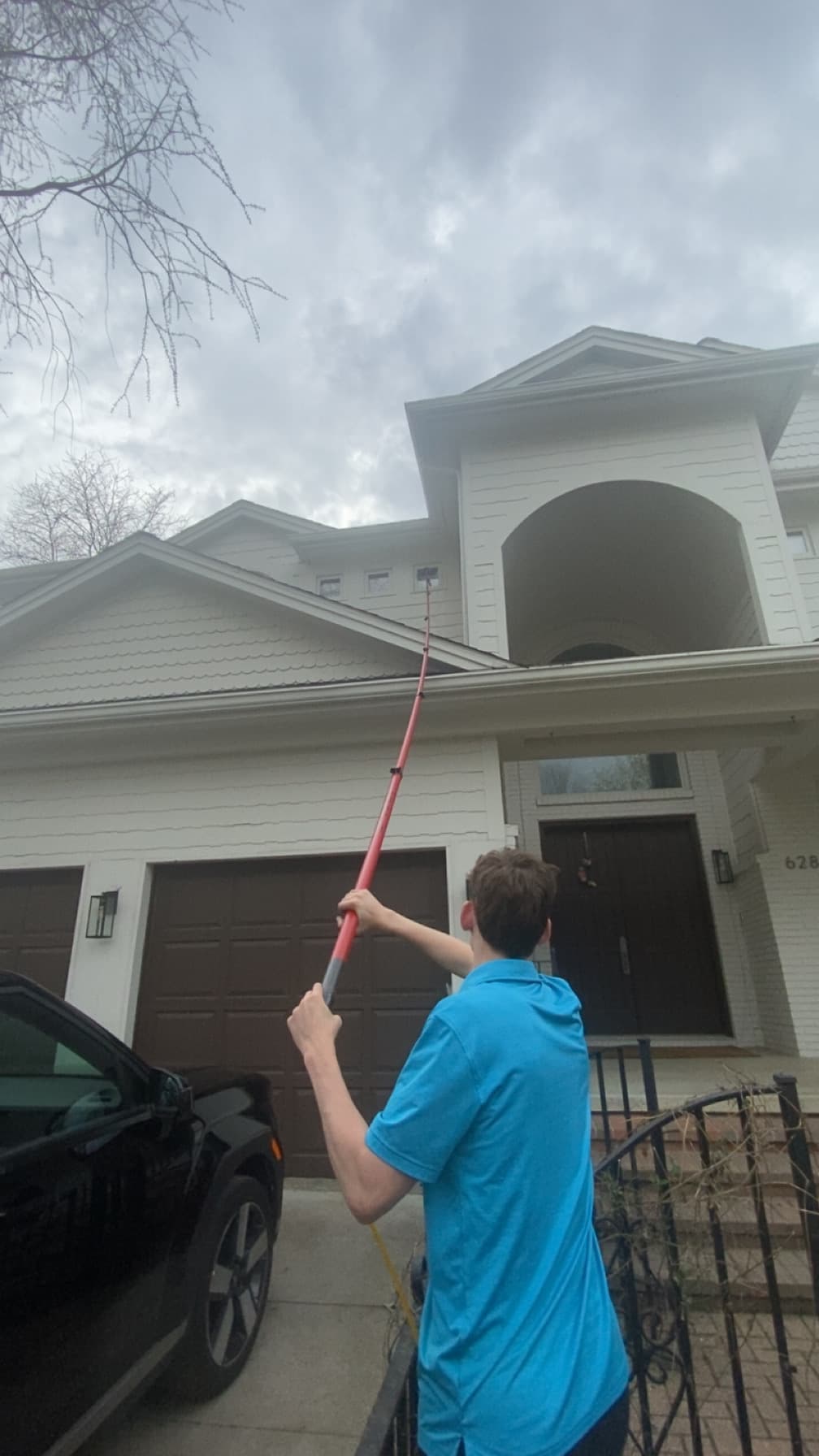 Super Shine Services technician using a water-fed pole to clean gutters and windows from the driveway of a home