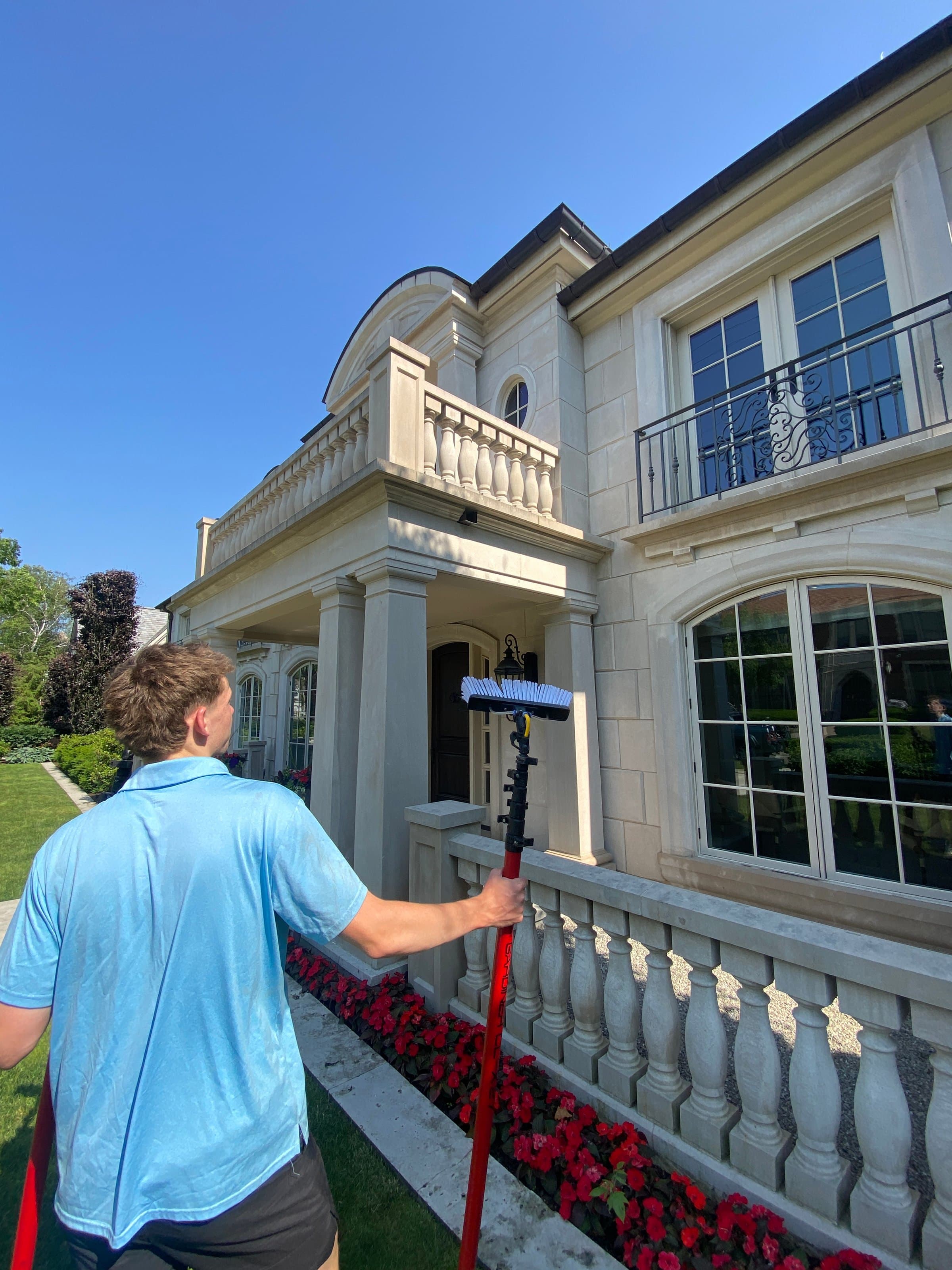 Super Shine Services technician cleaning windows on a stone estate with wrought iron balconies